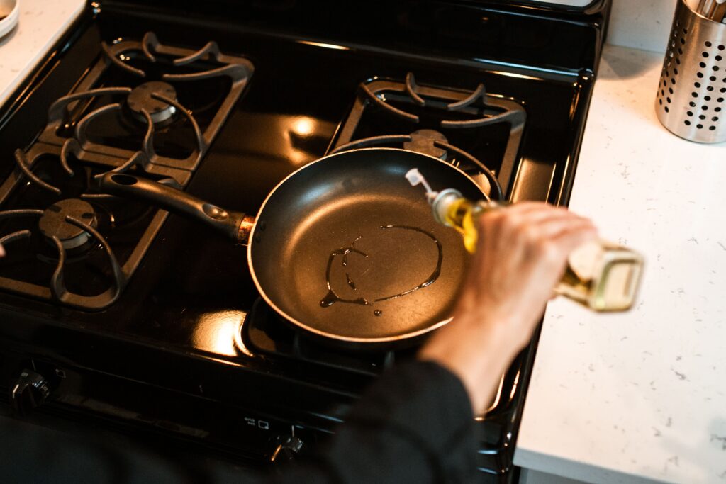 Cooking oil being poured into a hot frying pan on a stove for frying and sauteing