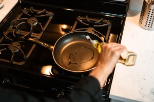 Cooking oil being poured into a hot frying pan on a stove for frying and sauteing
