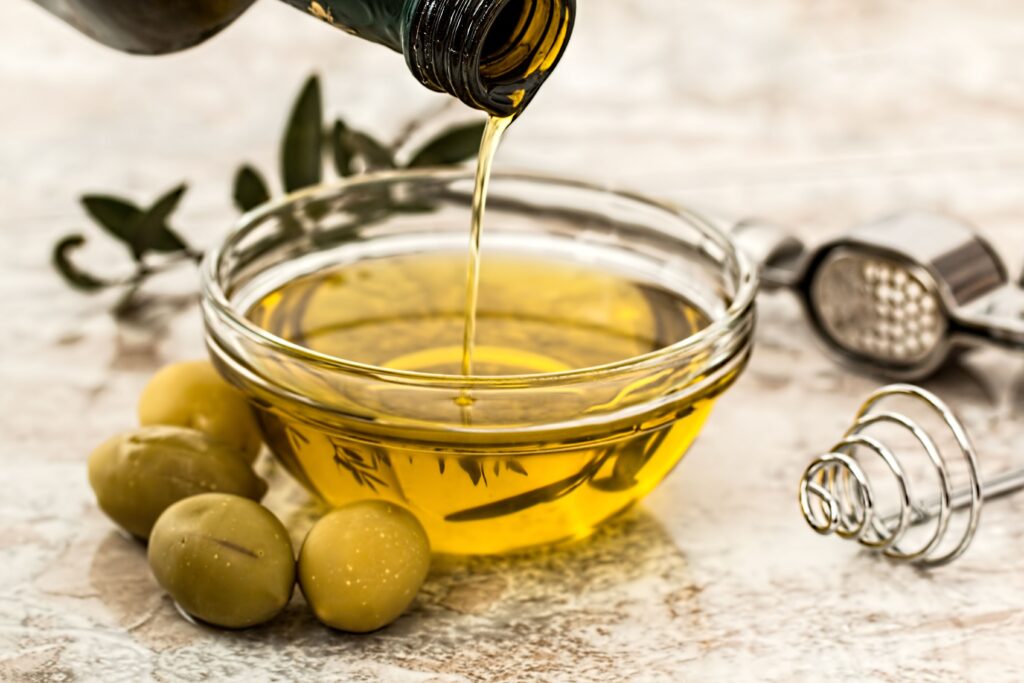 Extra virgin olive oil being poured into a bowl with olives for a salad dressing