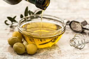 Extra virgin olive oil being poured into a bowl with olives for a salad dressing