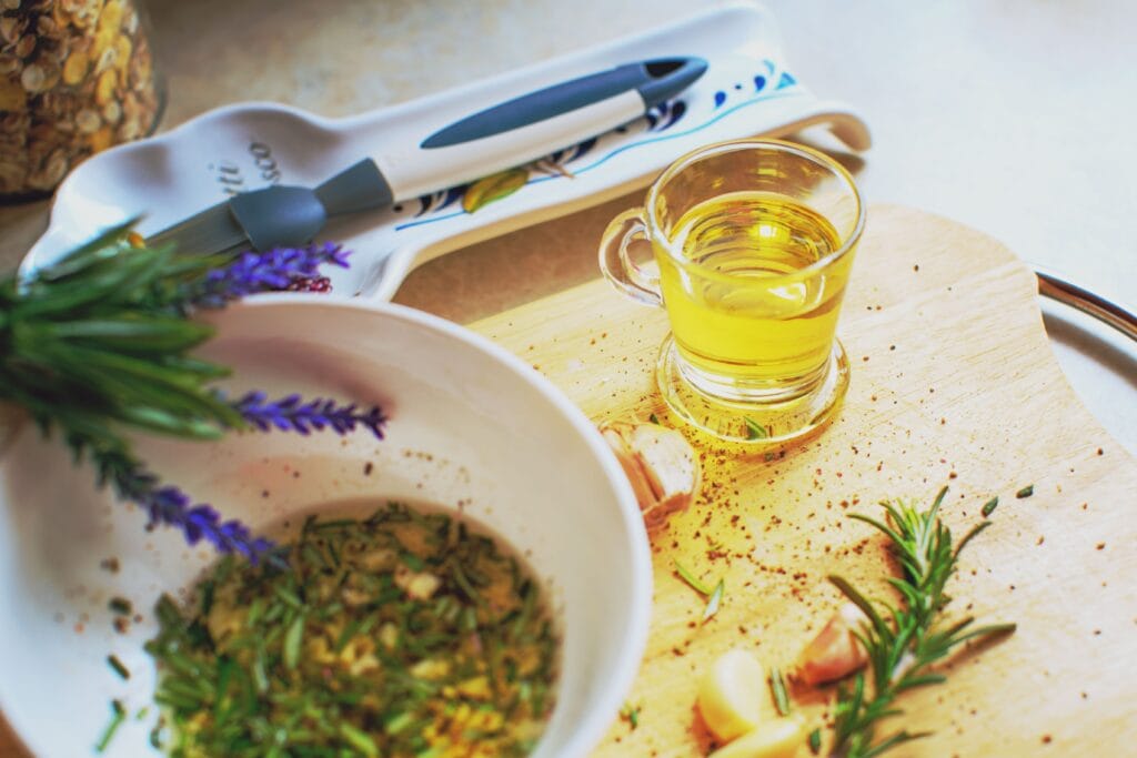 Glass jug of mustard oil beside ground mustard seed paste and herbs