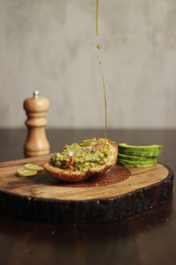 Oil being drizzled over avocado toast, representing healthy seed oil alternatives like avocado and olive oil